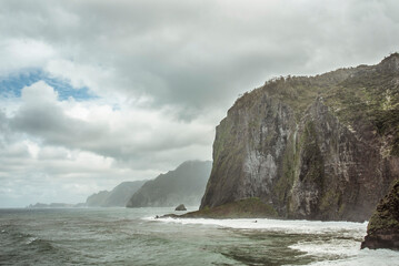 Fototapeta premium Furna do Porto da Cruz (Praia e Caís), Madeira Island, Portugal: Dramatic cliffs meet the ocean under a cloudy sky