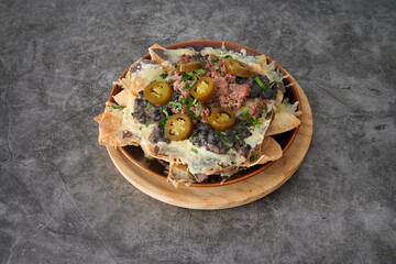 A plate of nachos with cheese and jalapenos. The plate is on a wooden board