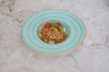 A blue plate with spaghetti and meatballs. The plate is on a marble counter. The spaghetti is covered in sauce and the meatballs are on top of the sauce