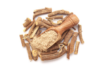 A wooden scoop filled with organic Liquorice or Mulethi (Glycyrrhiza glabra) powder, placed on a heap of liquorice roots, isolated on a white background.