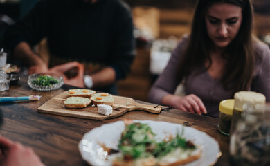 A group of individuals focusing on preparing appetizers at a wooden bar, showcasing a warm and inviting environment. The composition highlights teamwork and culinary creativity.