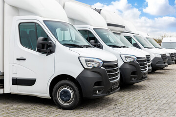 Fleet new modern electric hybrid hydrogen or diesel white vans parked in line row outdoors. Cargo freight industrial courier transportation logistics service. Commercial vehicle maintenance insurance