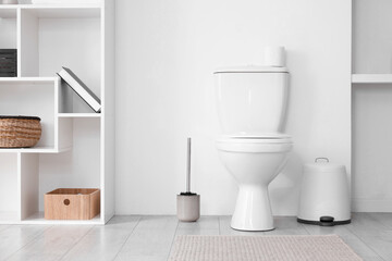 Toilet, brush and necessities near white wall in bathroom
