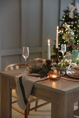 Christmas table setting with stylish dishware, glasses and burning candles in festive decorated room