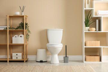 Toilet bowl, brush and necessities near beige wall in restroom
