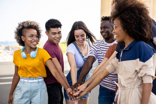 Diverse group of young people stacking hands together outside. Millennial student friends showing unity and cooperation. Teamwork concept