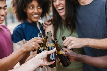 Happy multiracial friends having fun while cheering with beer at summer party. Friendship and celebration lifestyle concept