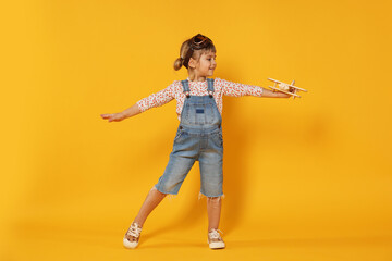 Happy little girl playing with toy plane on orange background