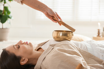 Woman undergoing singing bowl therapy lying on floor indoors