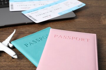 Passports, flight tickets, plane model and laptop on wooden table, closeup