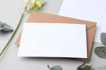 Blank greeting card, paper envelope, flower and eucalyptus leaves on light grey background, closeup