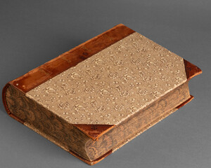 An antique book displayed against a neutral background, showcasing its rich wear and tear. The book's aged pages and cover highlight its historical significance and charm.