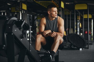 Tired fit man with a well built body takes a breather after an intense rowing machine workout in a...