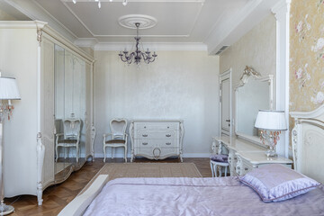 design of bedroom in retro style. interior with retro furniture. bedroom is decorated in beige and purple shades. double bed, wardrobe, chest of drawers, chair, mirror, windows with purple curtains.