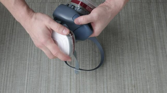 Man&rsquo;s hands inserting a filter into a protective respirator mask on a gray surface, close-up view.