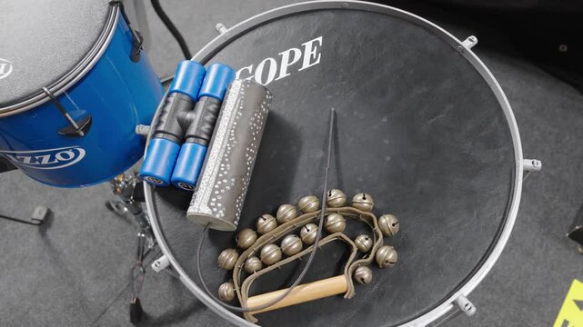  Various percussion instruments including a guiro, jingle bells, and blue shakers placed on a drumhead, captured in a studio setting.
