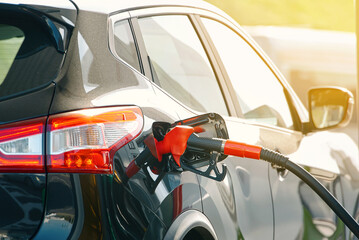 Gasoline nozzle at vehicle fuel tank during refueling at station. Closeup of fuel nozzle inserted into car at gas station, rising cost of fuel and its effect on consumer spending and mobility