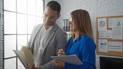 Man and woman collaborating in a bright office, reviewing documents and engaging in a discussion,...