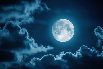 Full moon shines brightly in a dark blue night sky with clouds.