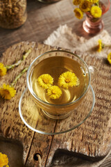 A cup of coltsfoot tea with fresh coltsfoot flowers on a wooden table