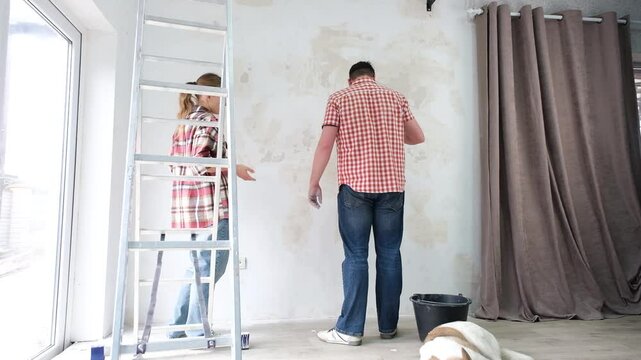 Happy couple renovating new house apartment , spackling wall, woman checking the bills surprised. Cute dog calmly sleeping in the foreground on the floor. Home makeover, renovation concept. Family man