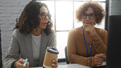 Hispanic women discussing work in an office interior, showcasing a diverse professional environment with coffee culture and teamwork dynamics.