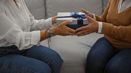 Mature women exchange gift in cozy living room symbolizing friendship and connection showcasing hispanic culture indoors enhancing warm home atmosphere and relationship bonds