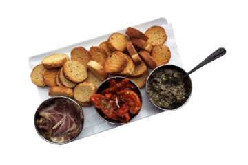 Starter dish with dried sweet tomatoes, black olive tapenade, meat slices and croutons in three bowls on rectangular plate, rustic traditional appetizer of French cuisine, restaurant menu