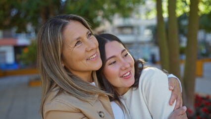 Mother and daughter embrace in a sunny urban park, showcasing love and family connection in a vibrant city environment.