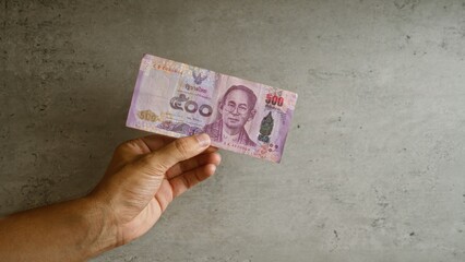 Hand holding thai baht banknote against concrete background in thailand, showcasing currency...