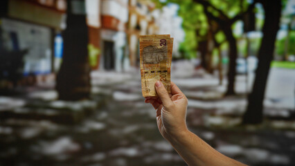 Hand holding south african rand banknote against urban outdoor street background, symbolizing...