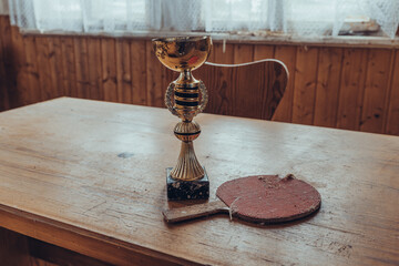 Old trophy and table tennis paddle showcased on wooden table in cozy indoor setting with natural...