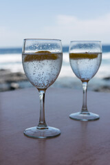 Two glasses of sparkling water with lemon on a beach. Aesthetic picture