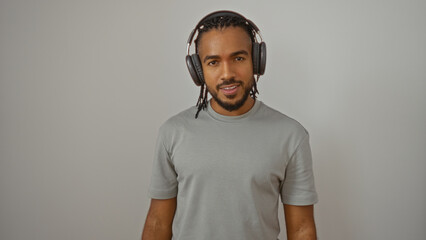 Young man with braided hair and headphones stands confidently against a plain white background, embodying an engaging and contemporary look.