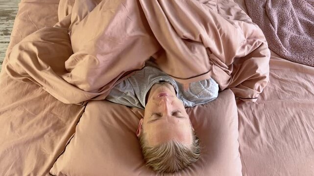 Man after sleeping snuggled within blanket while on a bed
