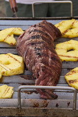 Whole cut of Lomo Fino, roasting on the grill accompanied by delicious slices of fresh pineapple