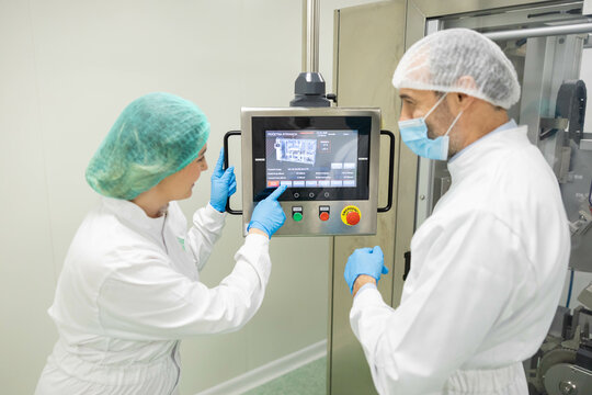 Focusing on a control panel, a technician and an operator ensure perfect settings for machinery in a clean supplement production