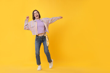 Emotional woman dancing on yellow background. Space for text