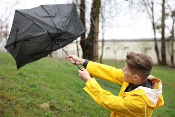 Man with broken umbrella fighting wind under rain outdoors