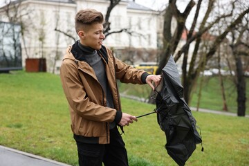 Man with broken umbrella fighting wind under rain outdoors