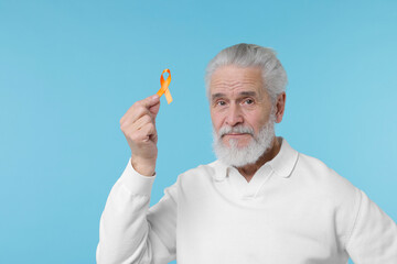 Multiple Sclerosis awareness. Senior man with orange ribbon on light blue background, space for text