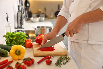 Professional chef cutting bell pepper at counter in kitchen, closeup