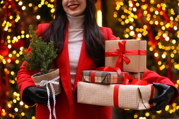 Woman with Christmas gifts and thuja tree on city street, closeup