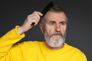 Obraz premium Handsome man combing his hair on dark grey background