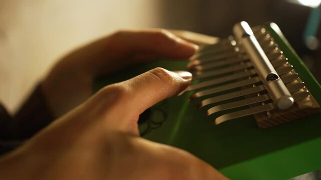 Skilled musician delicately plucking metal tines of green kalimba, creating soothing, mesmerizing melodies with gentle finger movements in intimate close-up