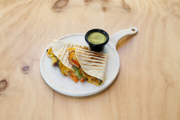 A plate of food with a tortilla wrap and a side of guacamole. The plate is on a wooden table