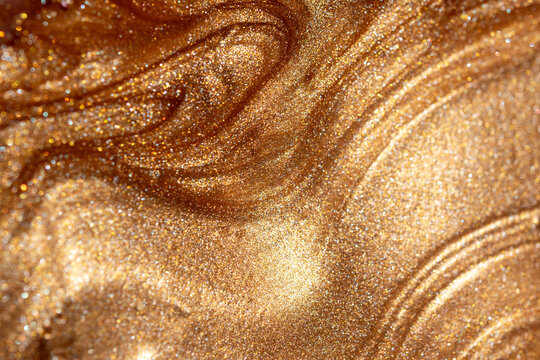 Texture background with golden shimmering cosmetic body spray or gel. Glowing backdrop.