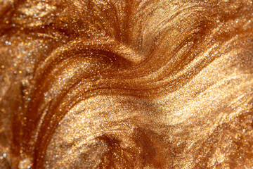 Close up view of golden shimmering cosmetic texture of gel or body spray. Background texture for backdrops or mapping.