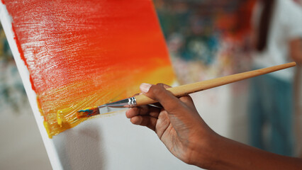 Closeup of african boy hand paint canvas with warm tone color while caucasian girl in casual outfit...