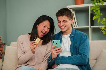 Excited couple enjoying online shopping together while laughing and engaging with their smartphones in a cozy living room, sharing moments of joy through mobile apps and credit card transactions